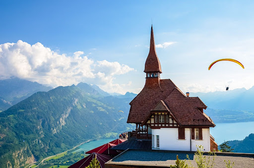 Stunning view of the top of Harder Kulm in Interlaken, Switzerland photographed in summer with paragliders flying around. Hilly Alpine landscape and Lake Thun in background. Paragliding, sunset